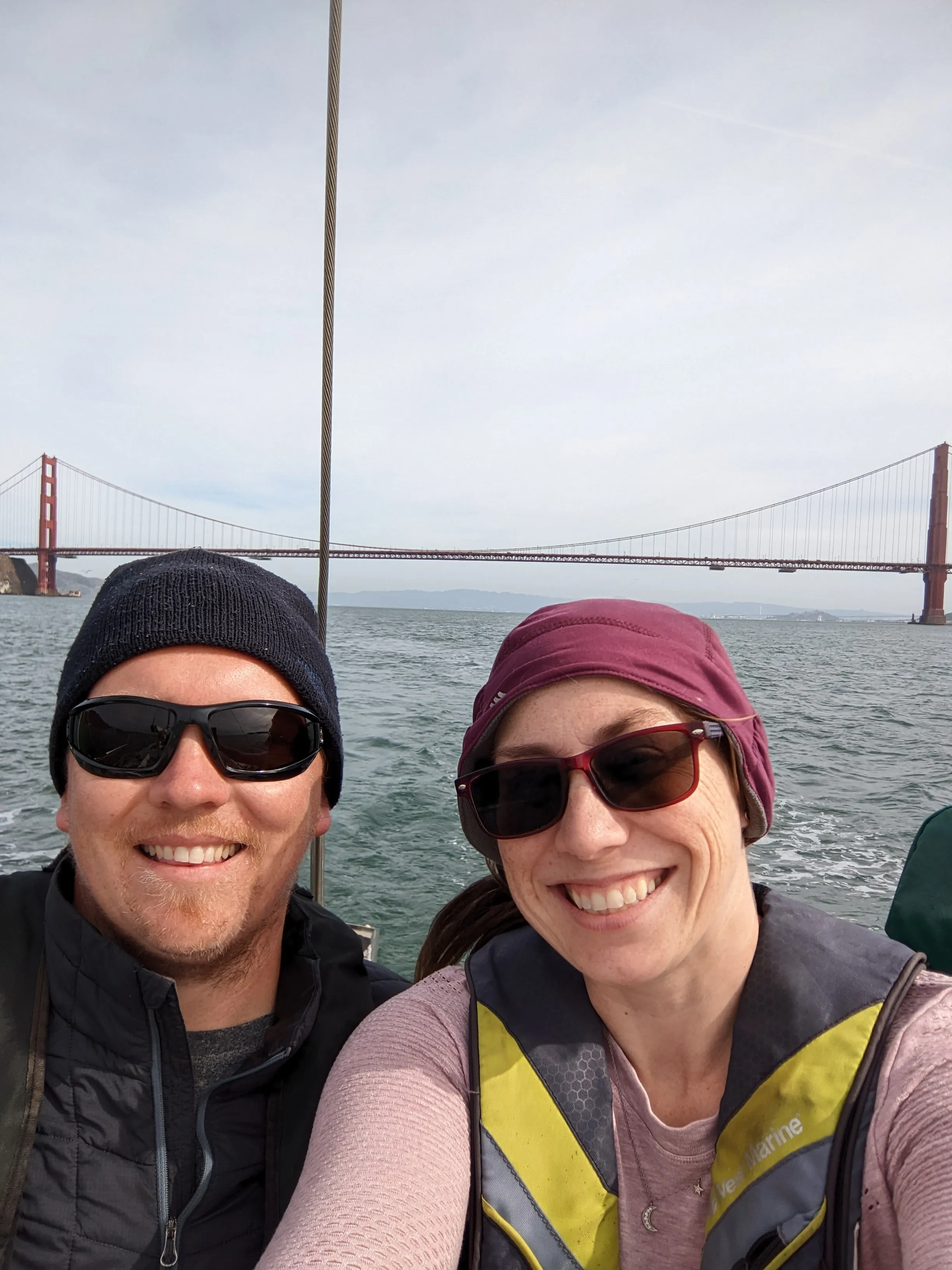 Alicia and Bryan smile after crossing under the Golden Gate Bridge, the Golden Gate in the background.